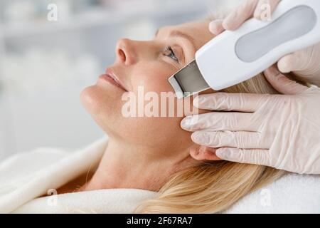 Primo piano donna anziana in salone di bellezza professionale durante la procedura di pulizia del viso ultrasonica. Trattamento viso, pulizia viso Foto Stock