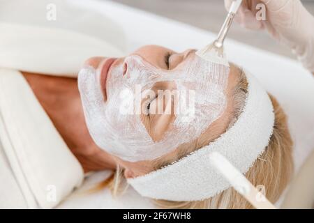 Primo piano foto di estetista che applica la maschera nutrizionale faccia donna anziana Foto Stock