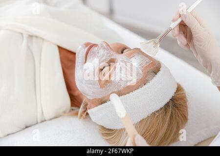 Primo piano foto di estetista applicando la maschera nutrizionale sul viso della donna anziana. Foto Stock