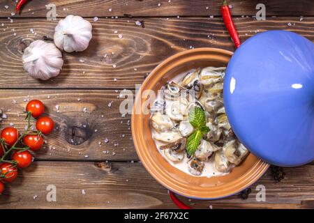 Gnocchi con salsa alla crema e funghi in una pentola di argilla su fondo di legno. Vista dall'alto. Foto Stock