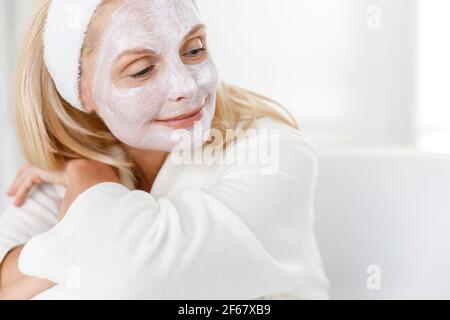 Primo piano di donna anziana con maschera nutrizionale sul viso, cosmetologi in visita nel moderno centro medico Foto Stock