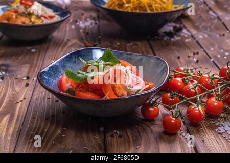 Pomodori affettati con cipolle in un piatto su fondo di legno marrone, decorati con pomodori ciliegini, sale grosso e piselli al pepe. Il concetto di healt Foto Stock
