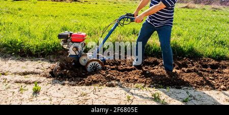 Un uomo aratura il terreno con una tillerblock nel giardino. Lavori agricoli. Foto Stock