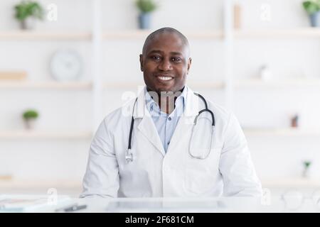 Ritratto della testa del medico allegro in bianco uniforme che consulta il paziente online, guardando la macchina fotografica, Foto Stock
