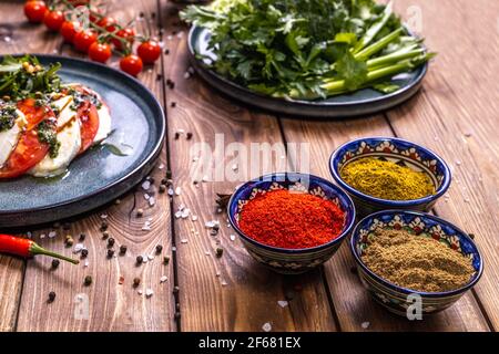 Pomodori con mozzarella, erbe fresche, peperoncini, spezie nell'assortimento su sfondo ligneo. Menu del ristorante. Foto Stock