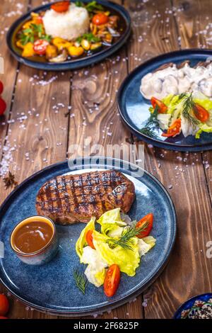 Bistecca con salsa, lattuga, rosmarino, pomodori ciliegini su tavola di legno. Layout piatto. Foto Stock