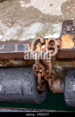 Una vecchia catena arrugginita che collega i paraurti a tubo in gomma sul molo del mare. Un frammento del molo. Foto Stock