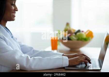 Alimentazione sana. Consulente di perdita del peso che scrive sul computer portatile, dando consultazione in linea al paziente alla clinica Foto Stock