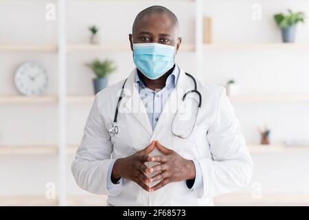 Concetto di salute e medicina. Ritratto di sicuro medico nero in maschera facciale, in posa a macchina fotografica in studio clinico Foto Stock