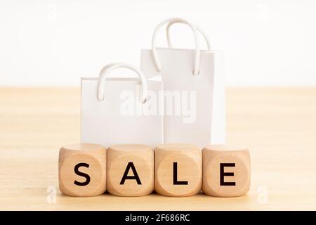 Concetto di vendita. Parola su blocchi di legno e sacchetti di carta bianca per la spesa sul tavolo. Sfondo bianco Foto Stock