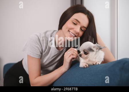 Bellissima donna felice che accarezzava il suo adorabile cane, rimanendo a casa Foto Stock