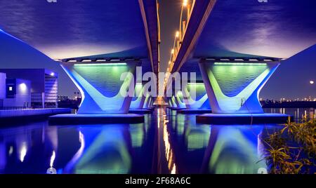 Splendida vista notturna invernale del famoso Ponte al Garhoud illuminato blu a Dubai, Emirati Arabi Uniti, con la colorata riflessione sull'acqua Foto Stock