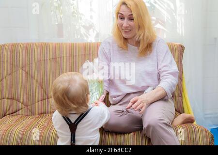 Il ragazzino si congratula con la madre per la vacanza, le dà fiori e un regalo. Ragazzo in camicia bianca e pantaloni con sospenditori Foto Stock