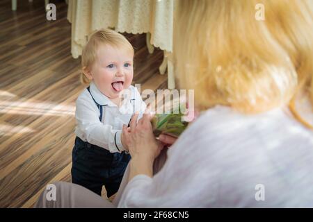 Il ragazzino si congratula con la madre per la vacanza, le dà fiori e un regalo. Ragazzo in camicia bianca e pantaloni con sospenditori Foto Stock