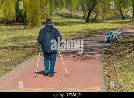 Un uomo anziano cammina in una giornata primaverile nel parco con bastoni per nordic walking Foto Stock