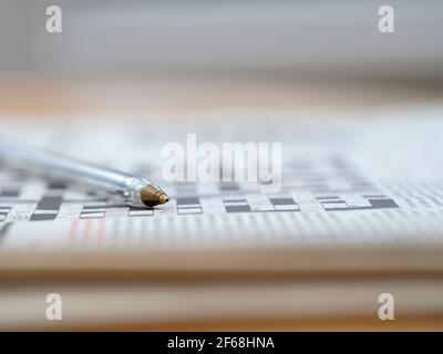Una penna biro poggia su una crossword parzialmente completata con le parole viste da un angolo basso. Foto Stock