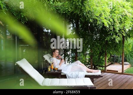 Donna che si rilassa al centro benessere. Rilassatevi in giardino. La giovane donna si rilassa seduta su un'amaca nel giardino verde. Foto Stock