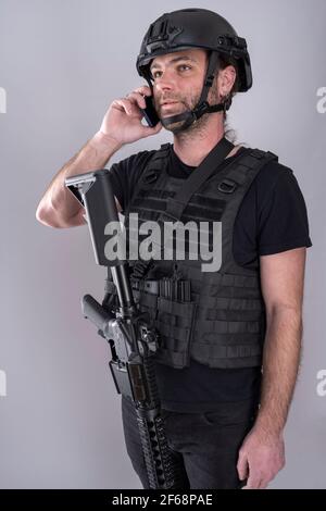 Uomo equipaggiato per Airsoft con casco e gilet protettivo sta confermando la strategia sul telefono mentre si sta in piedi con la sua arma visualizzata. Negociation Foto Stock