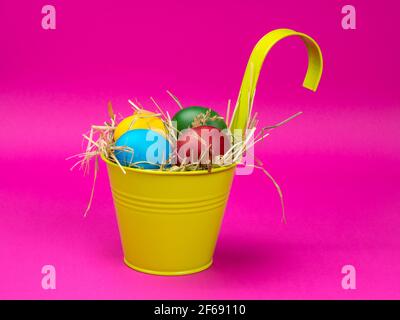 Uova di Pasqua sul fieno in un secchio luminoso. Sfondo rosa. Foto Stock