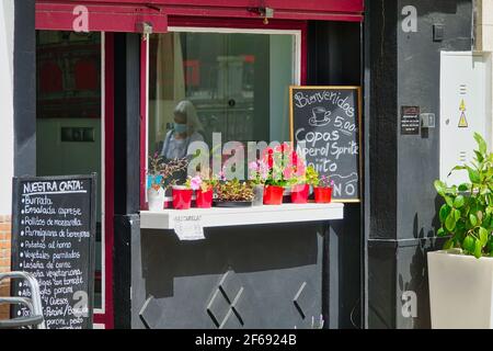 Ingresso di un ristorante di cucina italiana a Granada (Spagna) aperto al pubblico, con il riflesso di una donna con una maschera nella finestra Foto Stock