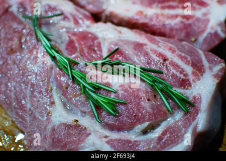 Bistecche di maiale fresche con rosmarino, salate su tavola di legno. Carne marmorizzata per grigliare. Messa a fuoco selettiva. Foto Stock