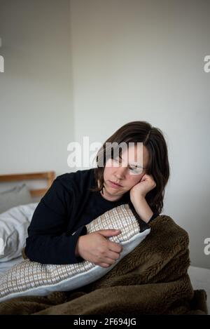 Donna seduta nel letto appoggiando la testa sulla mano guardando lontano Foto Stock