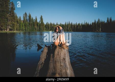 Bionda Donna pone su un ceppo sopra l'acqua al tramonto. Foto Stock