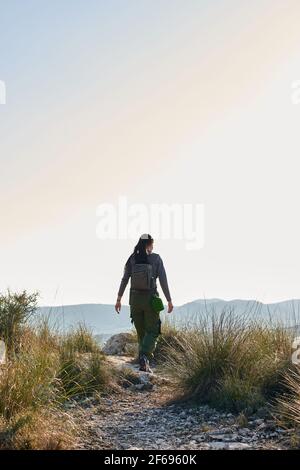 Una donna esploratrice cammina lungo una strada sterrata osservando la natura Foto Stock