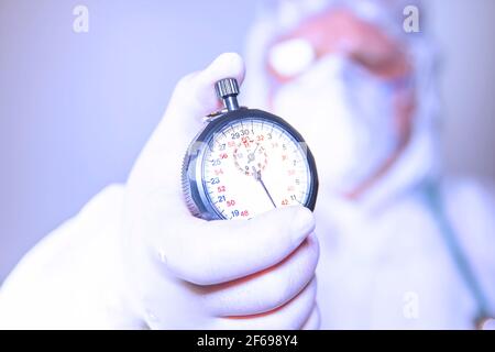 Un medico che indossa una maschera chirurgica e guanti chirurgici che tengono un cronometro per un'azione rapida per resistere alla diffusione della covid 19 e alla vaccinazione. Su sfondo bianco Foto Stock