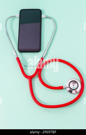 Vista dall'alto di uno stetoscopio in un auricolare per smartphone su sfondo verde acquamarina. Concetto di medicina, comunicazione e tecnologia. Foto Stock