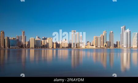 Vista panoramica dei raschiatori del cielo di sharjah che mostrano splendidi riflessi in acqua catturati durante l'alba della prima mattina dall'isola di al Noor Foto Stock