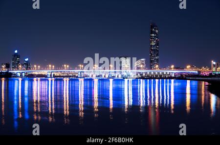 Splendida vista notturna del ponte illuminato Garhoud sull'acqua con riflessi, circondato da scrapper catturati dal Dubai Creek Park Foto Stock