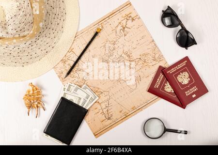 mappa del mondo, matita, due passaporti, occhiali da sole, conchiglia, Portafoglio nero con soldi e un cappello di paglia su un tavolo di legno bianco. Iscrizione - passaporto russo F Foto Stock