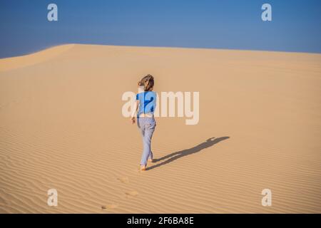 Giovane ragazzo che viaggia nel deserto. Dune sabbiose e cielo blu nella soleggiata giornata estiva. Concetto di viaggio, avventura, libertà. Il turismo riapre dopo la quarantena Foto Stock