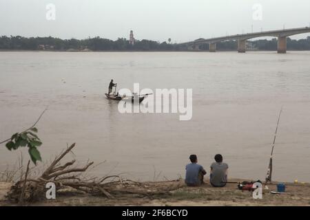 Giovani uomini che pescano dalla riva del fiume come passa una barca da pesca, galleggianti sul fiume Mekong a Kampong Cham, Cambogia. Un'adeguata 'governance delle acque' oltre i confini è fondamentale poiché dighe e sviluppo (ironicamente) minacciano l'ambiente e la vita di milioni di persone, ha scritto Paritta Wangkiat in un'analisi pubblicata da Bangkok Post il 25 marzo 2021. Foto Stock