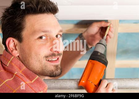 L'uomo facendo muretti a secco di lavorare sotto una pendenza del tetto Foto Stock