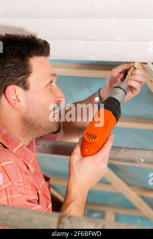 L'uomo facendo muretti a secco di lavorare sotto una pendenza del tetto Foto Stock