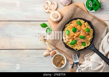 Pasta con funghi e basilico in padella su fondo chiaro. Foto Stock
