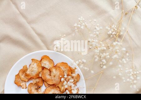 Fette di pere secche tagliate e mele su un bianco piatto e fiori secchi bianchi Foto Stock