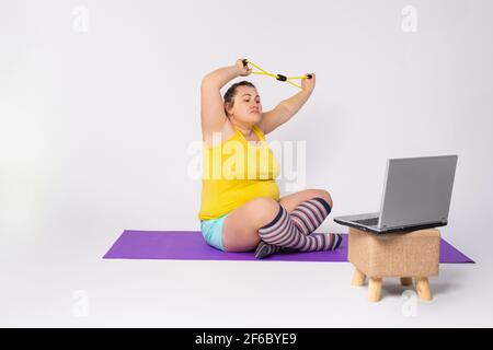 La ragazza caucasica si allena a casa. Attività sportive nel monolocale. Attrezzatura sportiva: Tappeto elastico per fitness. Formazione Chubby online Foto Stock