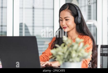 Donna asiatica come creatore di contenuti digitando su un podcast di ascolto portatile mentre si lavora da home.new stile di vita normale utilizzando la tecnologia Foto Stock