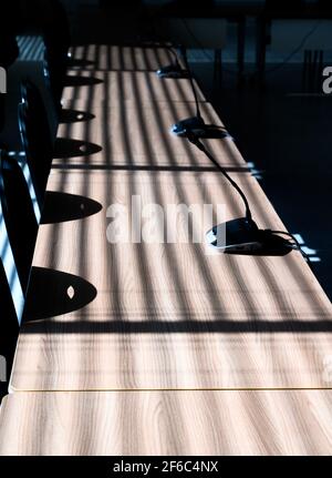 Vista ad alto angolo della fila di scrivanie in legno. Strisce d'ombra causate da persiane nelle finestre. Interno della prefettura di polizia Hauts-de-Seine edificio. Foto Stock