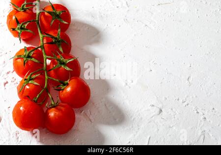 Bei pomodori freschi di vite (ciliegia) con gocce d'acqua, crudi, interi e dimezzati. Su sfondo bianco con texture. Ingredienti della dieta mediterranea Foto Stock