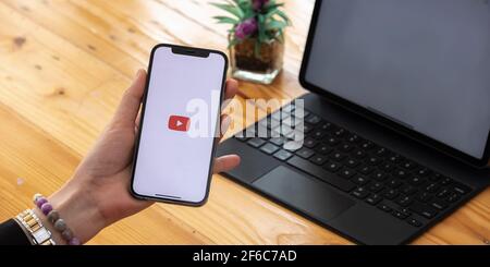 CHIANG mai, THAILANDIA - MAR 7, 2021: Mano donna che tiene Apple iPhone 12 con App YouTube fornisce streaming di contenuti multimediali e video sullo schermo Foto Stock