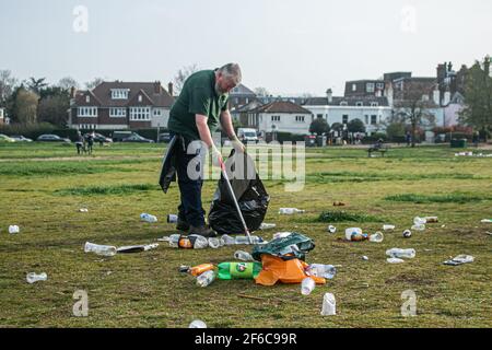 WIMBLEDON LONDRA, REGNO UNITO 31 MARZO 2021. Un operaio del merton council raccoglie i rifiuti su un sacchetto di bidone che include lattine di birra vuote e bottiglie di vino lasciate dai rivelatori su Wimbledon Common, in quanto le restrizioni di blocco sono state attenuate. Credit amer Ghazzal/Alamy Live News Foto Stock