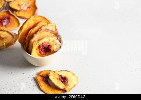 Frutta secca a fette patatine di pesca in ciotola su sfondo bianco con spazio per la copia. Primo piano. Snack vegan cibo senza zucchero. Foto Stock