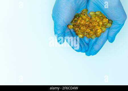 Le mani del medico in guanti medici blu contiene capsule gialle omega-3 medicinale, vitamine, pillola su sfondo blu con spazio di copia. Assistenza sanitaria, medica Foto Stock