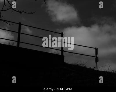 Moody fotografia in bianco e nero di un ponte ferroviario contro un cielo nuvoloso. Foto Stock