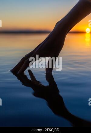 La mano delle ragazze tocca l'acqua calma o il lago Weyba, Sunshine Coast, Queensland, Australia Foto Stock