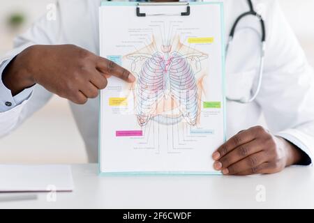 Medico che parla della malattia del coronavirus, mostrando immagine con il petto, i polmoni e l'organo respiratorio su blocco note Foto Stock